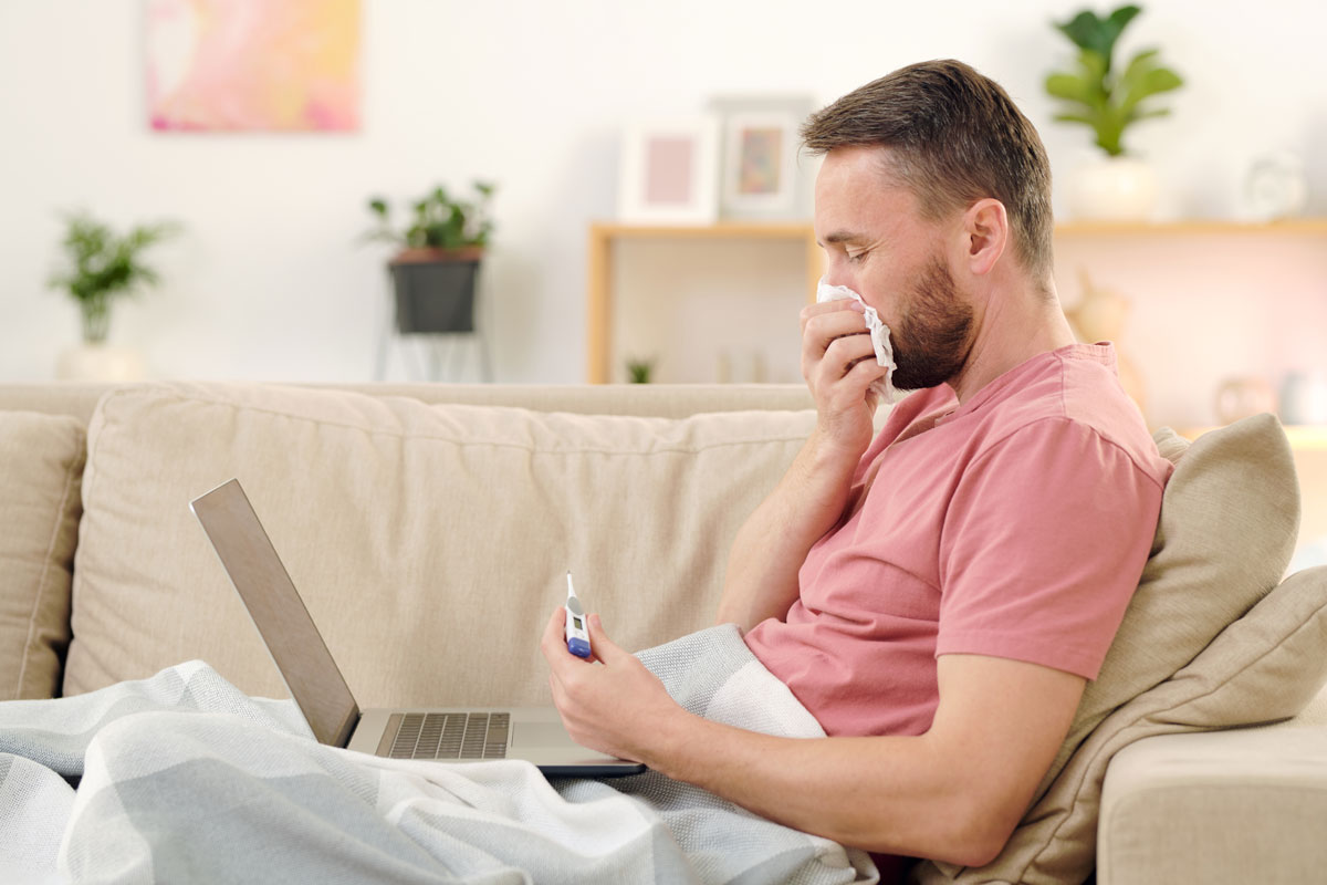 side view of young sick man looking at thermometer